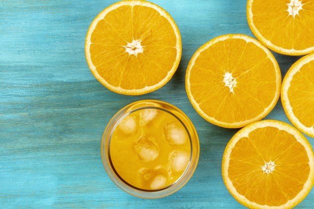A photo of a glass of fresh orange juice with orange halves, shot from above on a vibrant blue background with a place for text