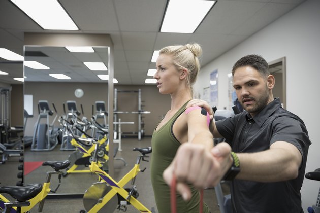 Male physiotherapist helping female client wearing elastic therapeutic tape stretching in clinic gym