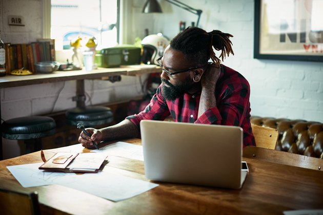 Male designer with tattoos drawing at desk.