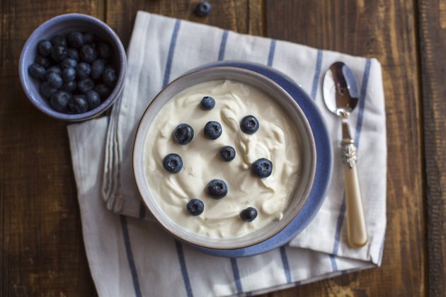 Yogurt with blueberries in bowl on wood