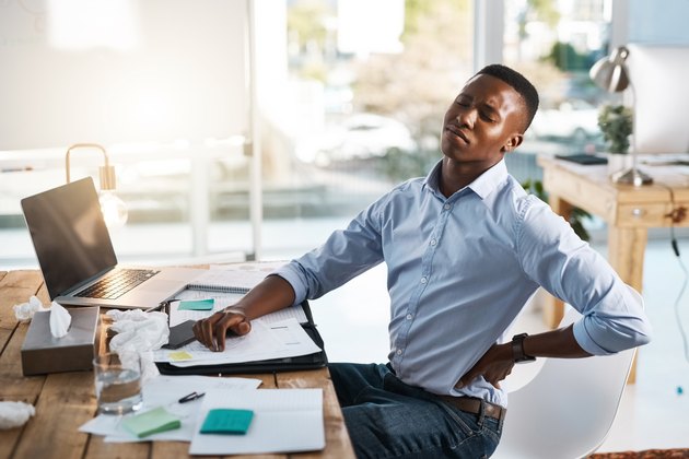 A man sitting at an office desk and holding his back in pain from poor posture