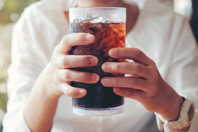 Close view of a woman's hands on a large glass of soda with ice