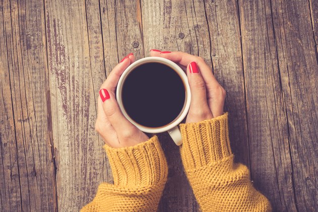 Female hands in warm sweater holding cup of coffee