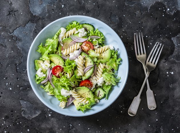 Mediterranean pasta avocado salad on a dark background, top view. Vegetarian diet food concept