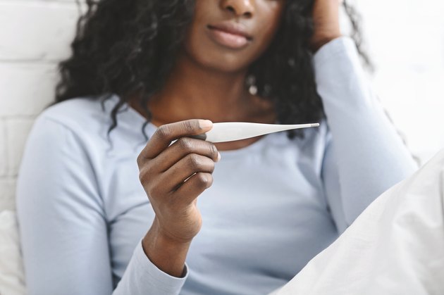 Sick woman with fever checking her temperature in bed