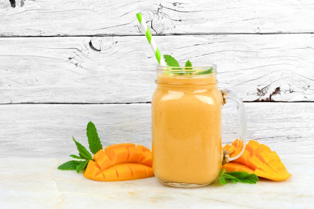 Mango coconut smoothie in a mason jar, on rustic white wood