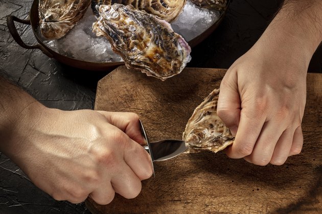 Shucking an oyster, man's hands holding a knife, opening oysters