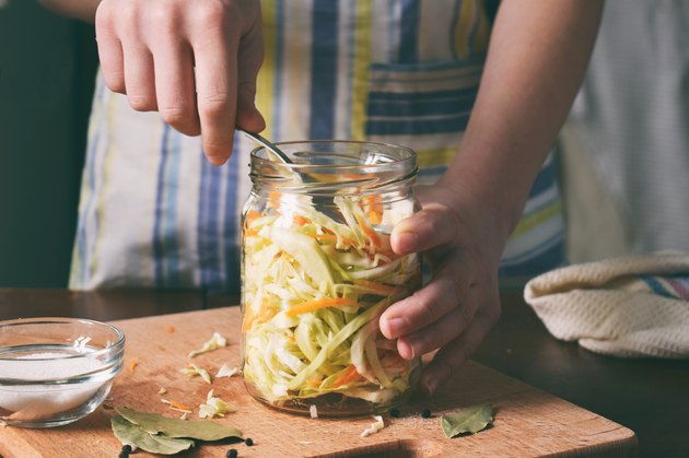 女人做饭木背景酸菜或沙拉。第5步 - 把白菜在罐子。发酵腌制蔬菜食品的概念。