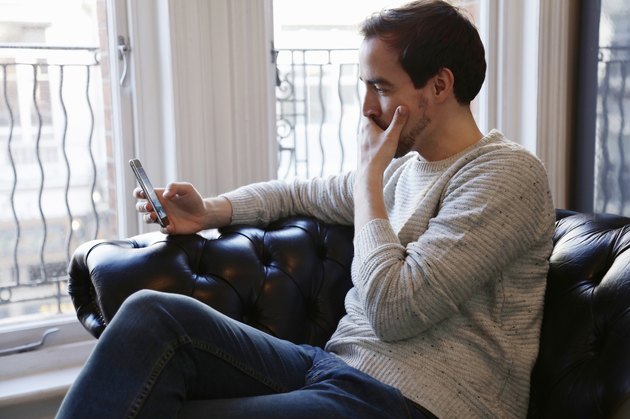 Mid adult man sitting on sofa, looking at smart phone