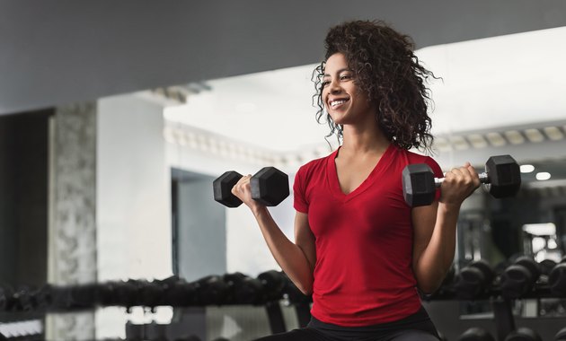 African-american fitness woman doing biceps workouts in gym
