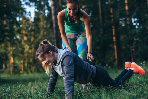 Sporty young female trainer showing a girl how to do knee push-ups while training outdoors in summer