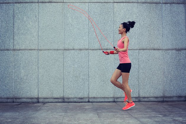 young fitness woman rope skipping against city wall