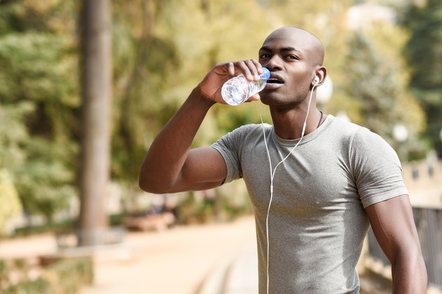 Young black man drinking water before running in urban background