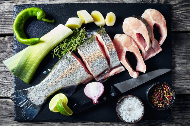 sliced raw trout with lime wedges, leek, thyme, salt and spices on a black stone cutting board