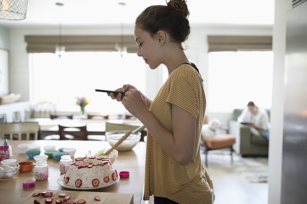 Teenage girl baking cake, photographing with camera phone
