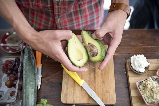 Young man holding halves of avocado in kitchen