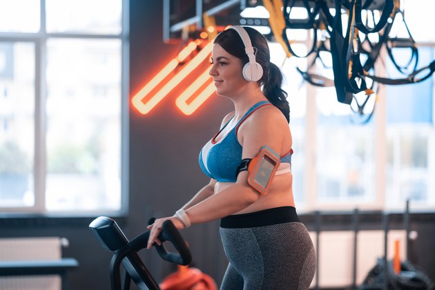 Woman cycling in gym and listening to music in earphones