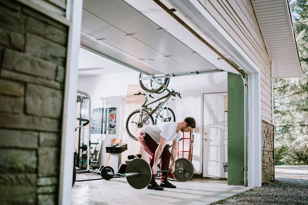 Man lifting barbell to build muscle in garage