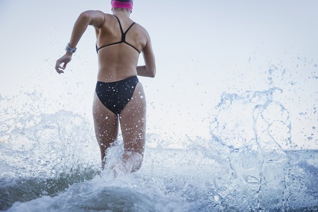 Female open water swimmers running and splashing in ocean surf