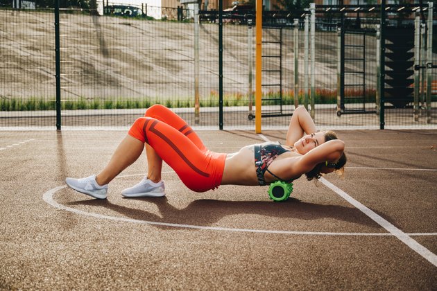 theme sport and rehabilitation sports medicine. Beautiful strong slender Caucasian woman athlete uses foam roller green field street workout to workout to remove pain, stretch and massage muscles