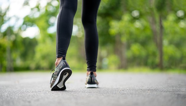 Runner feet running on road closeup on shoe. Young fitness woman runner athlete running at road. Athlete runner feet running on road closeup on shoe. Woman fitness sunrise jog workout wellness concept