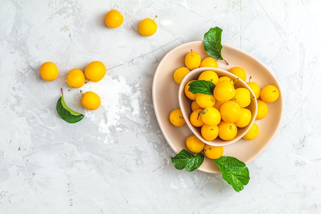 Creative summer pattern made of fresh yellow cherry plums in pink bowl on gray concrete background.