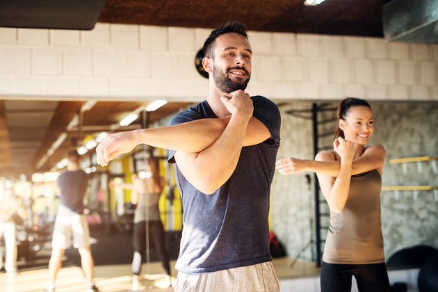 Strong young smiling athletes stretching in a gym .