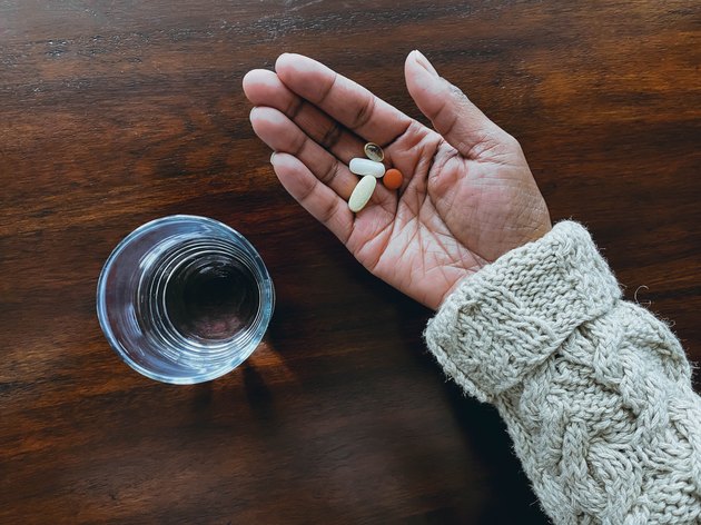 Woman Holds Daily Dose of Pills Next to Glass of Water