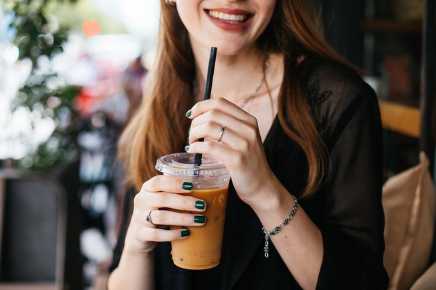 A smiling woman holding an iced coffee with a plastic straw
