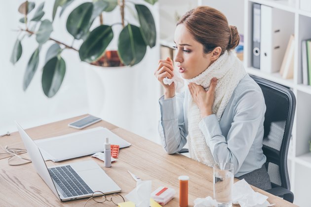 adult ill businesswoman with cough sitting at workplace in scarf