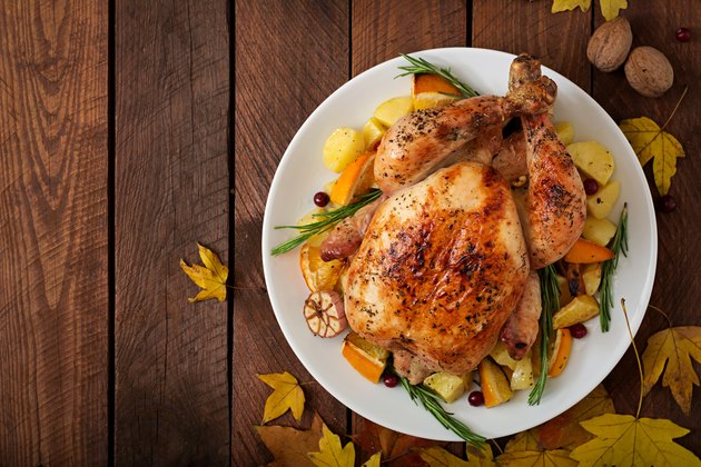 Roasted turkey garnished with cranberries on a rustic style table decorated with pumpkins, orange, apples and autumn leaf. Thanksgiving Day. Flat lay. Top view