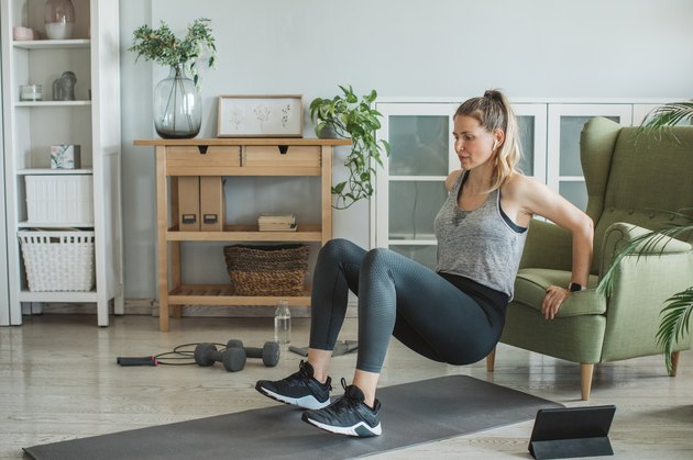 Woman doing triceps dips from a chair in her living room during an at-home workout
