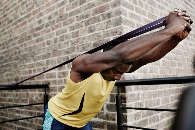 Man doing an overhead triceps extension with resistance band against a brick wall