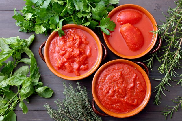 Canned tomatoes in bowls on background