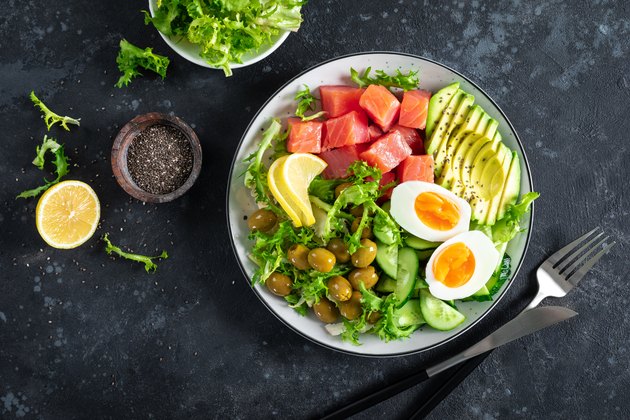 Ketogenic, paleo diet lunch bowl with salted salmon fish, lemon, avocado, olives, boiled egg, cucumber, green lettuce salad and chia seeds, healthy food trend, top view