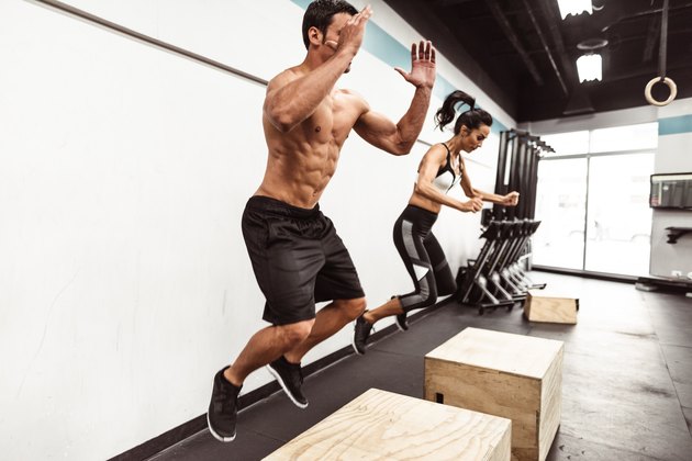 Man and woman doing box jumps at the gym as part of a HIIT workout.