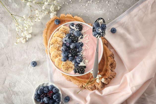 Bowl with pink yogurt and fresh fruits on light table