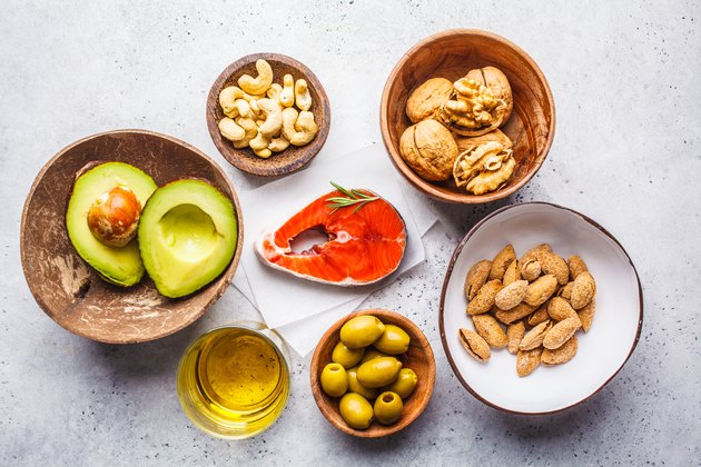 Top view of a variety of foods with healthy fats, including fish, nuts, oil, olives and avocado