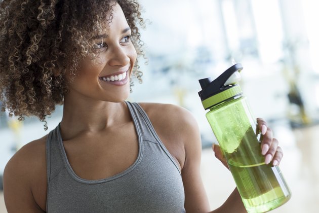 一个女人在健身房用绿色的塑料水瓶喝水