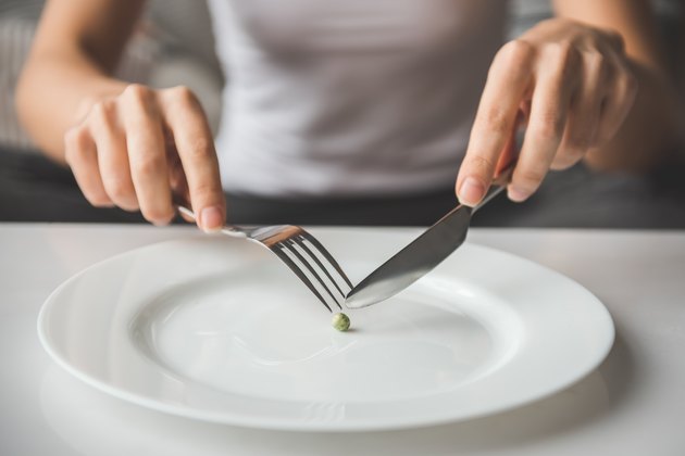 一位妇女正在用刀叉切豌豆;饮食概念