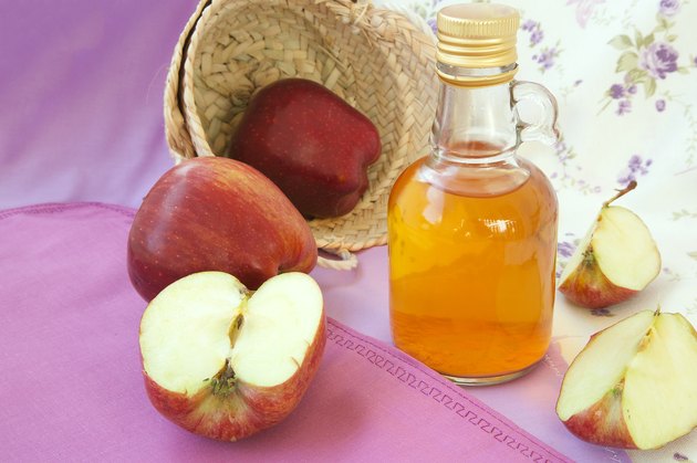 Apple cider vinegar in a bottle with apples on pink background
