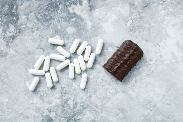 High Protein bar and Arginine capsules. Bodybuilding food supplements on bright stone background. Directly Above. Copy space.