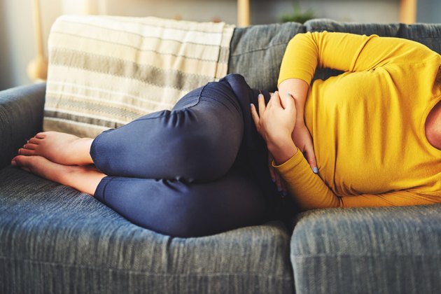 一个女人与肠易激综合征躺在沙发上，抱着她的胃疼痛