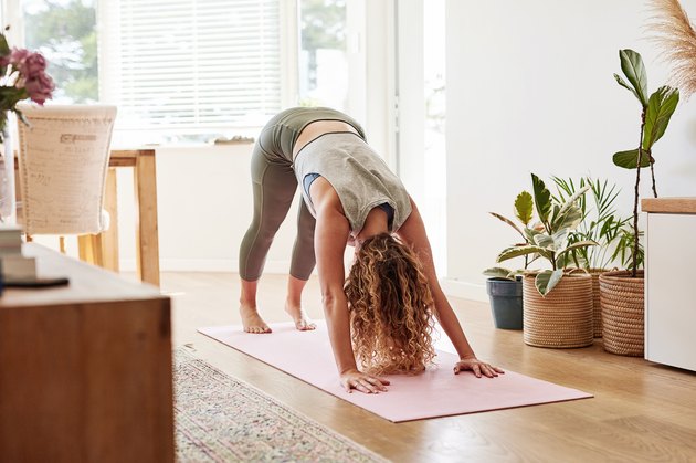 女人做向下在家里的粉红色垫面对狗Ashtanga瑜伽姿势