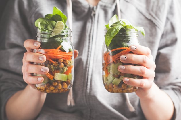 A woman holds and eats a salad in a glass jar with baked chickpeas, guacamole and vegetables. Healthy diet detox vegan food concept.