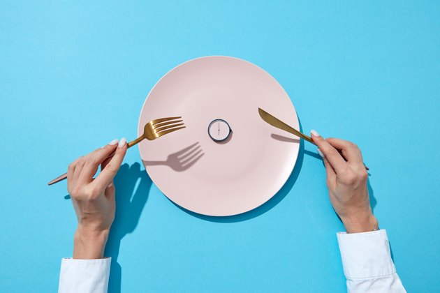 圆艳记显示六点钟白盘供应刀叉在一个女孩的手在蓝色背景。吃的时候和饮食观念。顶视图。