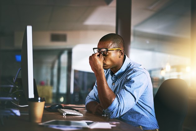 A stressed man sitting at his desk at work and rubbing his eyes