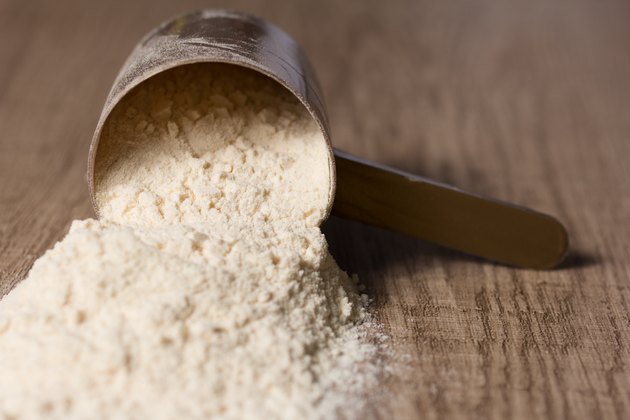 Whey Protein. Dropped scoop with vanilla powder flavour. Wooden table.