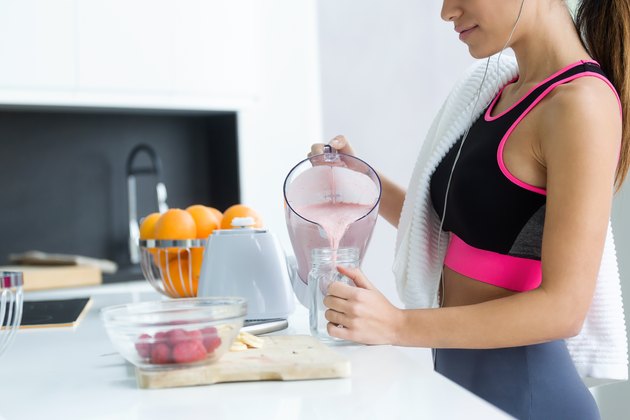 Sporty young woman serving strawberry protein shake in a glass jar in the kitchen at home.