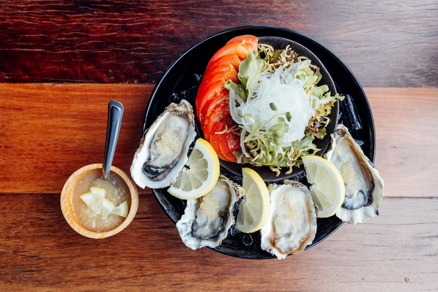 Fresh Oysters close-up on black plate, served table with oysters, lemon, ice and salad.